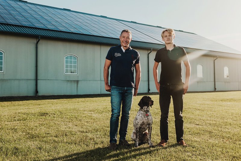 Stall mit Solaranlage und zwei Männern und einem Hund vor dem Stall.(was kann ich mit einer Photovoltaik-Inselanlage betreiben?)