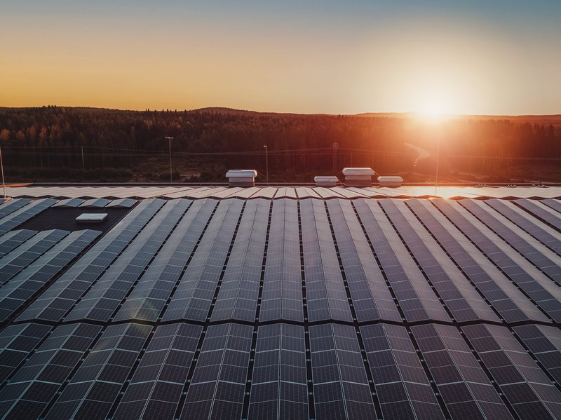 Solaranlagen auf dem Dach eines großen Unternehmens mit Sonnenuntergang im Hintergrund.